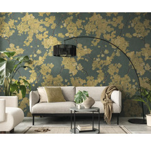 Woonkamer met vliesbehang met floraal patroon, gele bloesems op donkergroene achtergrond, lichtgrijze bank en zwarte booglamp.