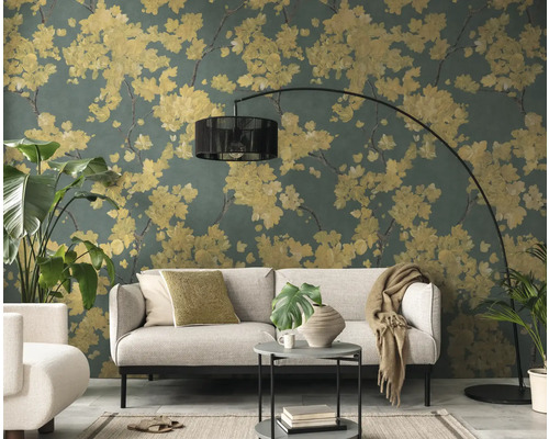Woonkamer met vliesbehang met floraal patroon, gele bloesems op donkergroene achtergrond, lichtgrijze bank en zwarte booglamp.