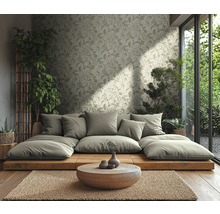 Lichte woonkamer met vliesbehang met bladmotief, lage houten platformbank, ronde houten tafel, jutemat en kamerplanten.