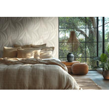 Helder ingerichte slaapkamer met behang in bladmotief, een bed met linnen bekleding, groot raam en natuurlijke decoratieve elementen.