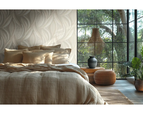 Helder ingerichte slaapkamer met behang in bladmotief, een bed met linnen bekleding, groot raam en natuurlijke decoratieve elementen.