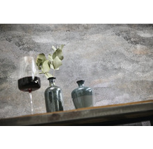 Wand in betonlook structuur met decoratie bestaande uit wijnglas, vaas met plant en pot op een houten plank.