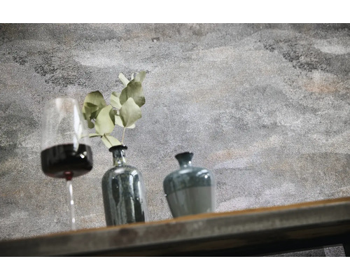 Wand in betonlook structuur met decoratie bestaande uit wijnglas, vaas met plant en pot op een houten plank.