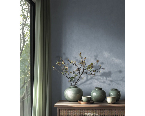 Drie groene keramieken vazen met craquelé glazuur en een bloeiende tak op een houten dressoir tegen een getextureerde blauwgrijze muur.