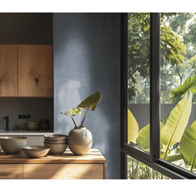 Moderne keuken met houten kasten, keramisch servies op houten werkblad, gestructureerde wand en groot raam met uitzicht op planten.