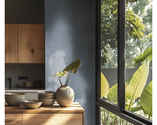 Moderne keuken met houten kasten, keramisch servies op houten werkblad, gestructureerde wand en groot raam met uitzicht op planten.