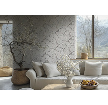 Vliesbehang met een fijn takken- en bloemenpatroon op een wand in een lichte woonkamer achter een bank met kussens.