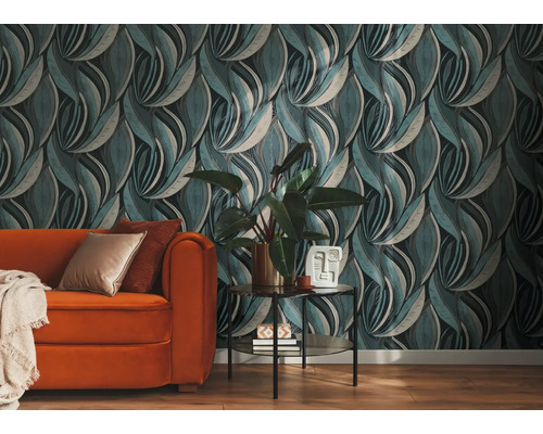 Vliesbehang met golvend bladmotief in een woonkamer met een oranje bank en kamerplant.