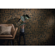 Wanddecoratie met geometrisch behang in bruin en zwart, een bruine leren fauteuil met kussen en een kamerplant op een bijzettafeltje.