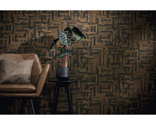 Wanddecoratie met geometrisch behang in bruin en zwart, een bruine leren fauteuil met kussen en een kamerplant op een bijzettafeltje.