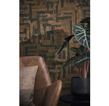 Vliesbehang met abstract geometrisch patroon in weefoptiek achter een bruine leren fauteuil en een kamerplant.