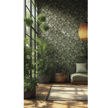 Vliesbehang met tropisch bladpatroon in groen en crème in een lichte kamer met kamerplanten, groene bank en gevlochten hanglamp.
