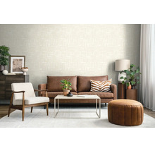 Moderne woonkamer met crème structuurbehang, bruine leren bank, witte fauteuil en een ronde leren poef.