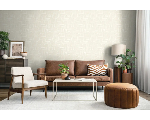 Moderne woonkamer met crème structuurbehang, bruine leren bank, witte fauteuil en een ronde leren poef.