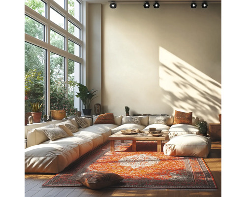 Lichte woonkamer met grote modulaire bank, houten salontafel en oosters tapijt voor een grote raampartij met plafondspots.