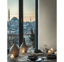 Gedekte tafel met keramische vazen, glazen en kaarsen voor een raam met uitzicht op een stad met moskeeën bij schemering.
