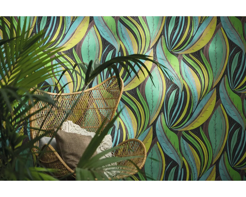 Vliesbehang met abstract bladerpatroon achter een rotan stoel met kussens en een kamerplant.