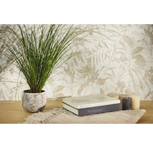 Vliesbehang met botanisch bladpatroon in lichte tinten, gecombineerd met een kamerplant, boeken en kaarsen op een houten tafel.