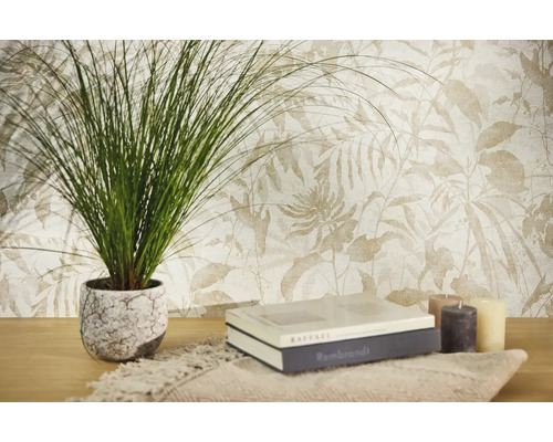 Vliesbehang met botanisch bladpatroon in lichte tinten, gecombineerd met een kamerplant, boeken en kaarsen op een houten tafel.