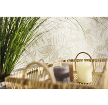 Vliesbehang met licht botanisch bladpatroon achter een decoratieve mand met kaarsen en groene grassen.