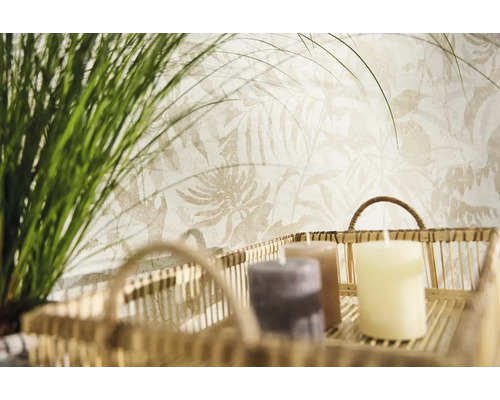 Vliesbehang met licht botanisch bladpatroon achter een decoratieve mand met kaarsen en groene grassen.