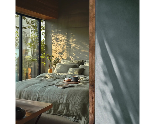 Moderne slaapkamer met groen linnen beddengoed, groot raam met uitzicht op groen en natuurlijk licht met schaduwen van planten op de muur.