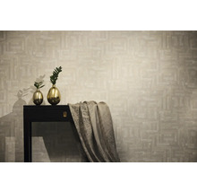 Vliesbehang met abstract geometrisch patroon in beige, gepresenteerd in een modern interieur met donkere sidetable en gouden vazen.