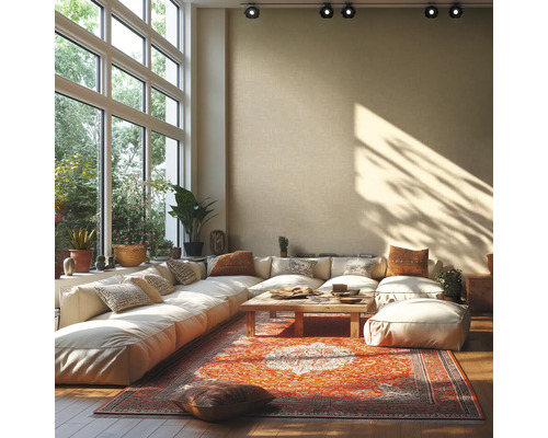 Lichte woonkamer met grote hoekbank, houten tafel en kleurrijk oosters tapijt voor een grote raampartij met uitzicht op groen.