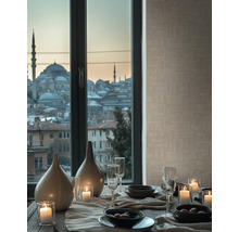 Gedekte tafel met keramische vazen, brandende kaarsen en glazen voor een raam met uitzicht op de stad en beige gestructureerd behang.