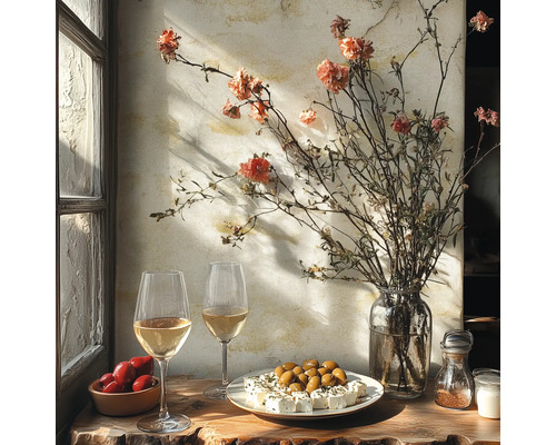Rustieke tafel bij het raam met witte wijn, olijven, feta, tomaten en een vaas met droogbloemen tegen een getextureerde muur.