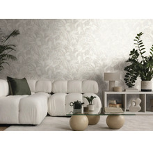 Moderne, lichte woonkamer met vliesbehang met bladmotief, modulaire bank, glazen tafel en kamerplanten.