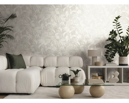 Moderne, lichte woonkamer met vliesbehang met bladmotief, modulaire bank, glazen tafel en kamerplanten.