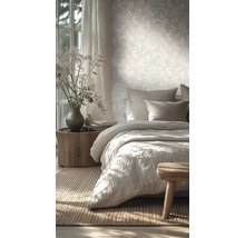Lichte slaapkamer met vliesbehang met bladmotief, een bed met linnen beddengoed en een nachtkastje van een boomstam.