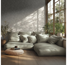 Moderne woonkamer met modulaire bank, veel kussens, behang met patroon, houten vloer, gevlochten poef en planten bij het zonnige raam.