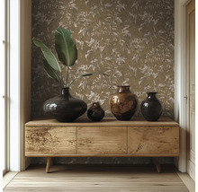 Houten dressoir voor een muur met behang met bladmotief, gedecoreerd met verschillende donkere vazen en grote groene bladeren.