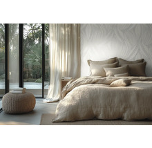 Licht ingerichte slaapkamer met vliesbehang met bladmotief, bed met linnen beddengoed en uitzicht door een glazen pui op de tuin.