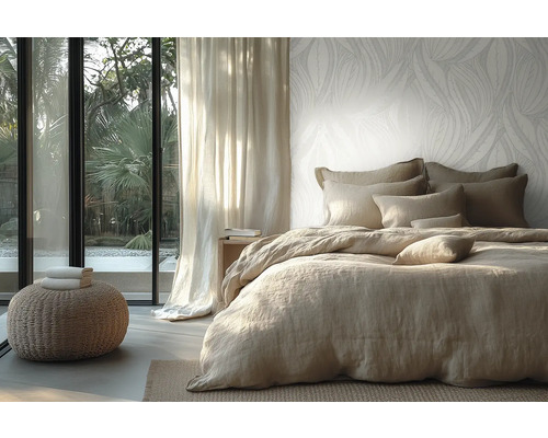 Licht ingerichte slaapkamer met vliesbehang met bladmotief, bed met linnen beddengoed en uitzicht door een glazen pui op de tuin.