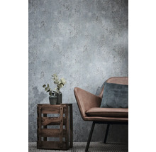 Vliesbehang met betonlook in de woonkamer met een stoel van imitatieleer en een houten krat als bijzettafel.