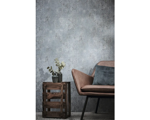 Vliesbehang met betonlook in de woonkamer met een stoel van imitatieleer en een houten krat als bijzettafel.