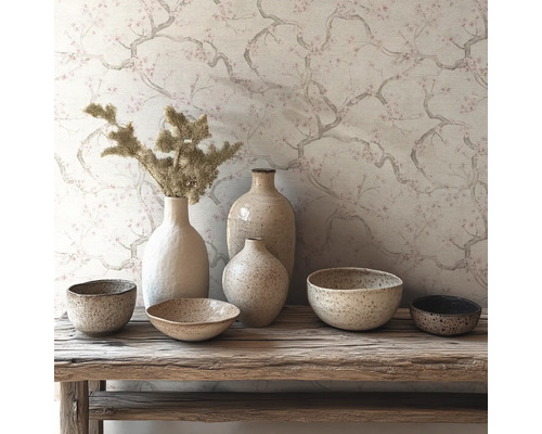 Behang met fijn takken- en bloesempatroon achter een compositie van keramieken vazen en schalen op een rustieke houten bank.