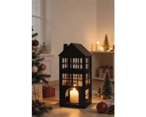 Zwarte metalen lantaarn in de vorm van een huis met een brandende kaars in een kerstscène met een versierde boom en cadeaus.