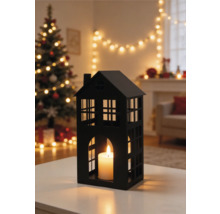 Zwarte lantaarn in de vorm van een huis met brandende kaars in een sfeervolle woonkamer met kerstboom en kerstverlichting.