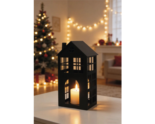 Zwarte lantaarn in de vorm van een huis met brandende kaars in een sfeervolle woonkamer met kerstboom en kerstverlichting.