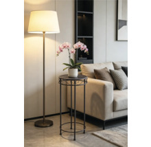 Moderne metalen plantenstandaard met een roze orchidee in een lichte woonkamer naast een beige bank en een vloerlamp.