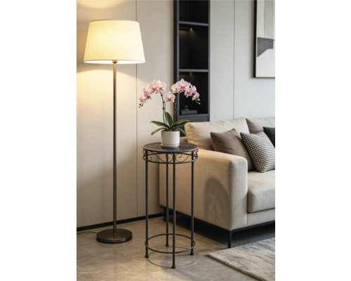 Moderne metalen plantenstandaard met een roze orchidee in een lichte woonkamer naast een beige bank en een vloerlamp.