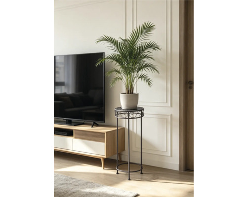 Hoge plantenstandaard van metaal met een palm in pot naast een tv-meubel in een lichte woonkamer.