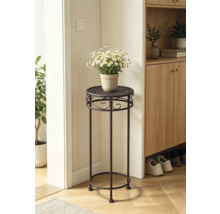 Hoge plantenstandaard van donker metaal met decoratieve ornamenten en witte bloemen in een lichte kamer naast een houten kast.