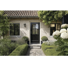 Huisingang met een zwarte voordeur met ruiten, lichte bakstenen muur, zwarte ramen en een bestraat pad door een tuin met hagen.