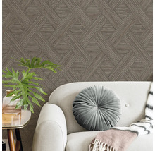 Bruin behang met geometrisch patroon achter een grijze bank met een rond fluwelen kussen en een kamerplant.