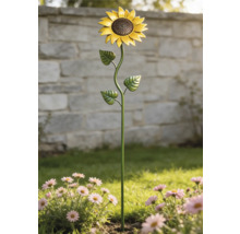 Tuinsteker zonnebloem van metaal in een bloembed met roze bloemen voor een stenen muur.